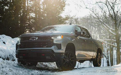 Chevrolet Silverado Trail Boss off-road pickup truck driving on a snowy mountain road in winter.